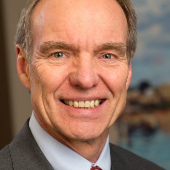 A man with short gray hair wearing a gray suit smiles for the camera.