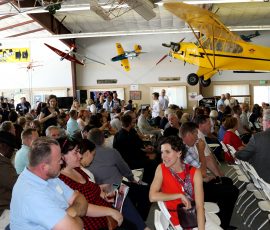 A large group of people gather inside a Museum of Flight facility