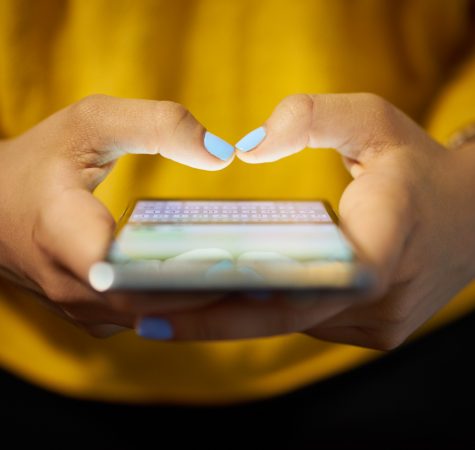 A close up photo of hands with blue nail fingernails holding a phone