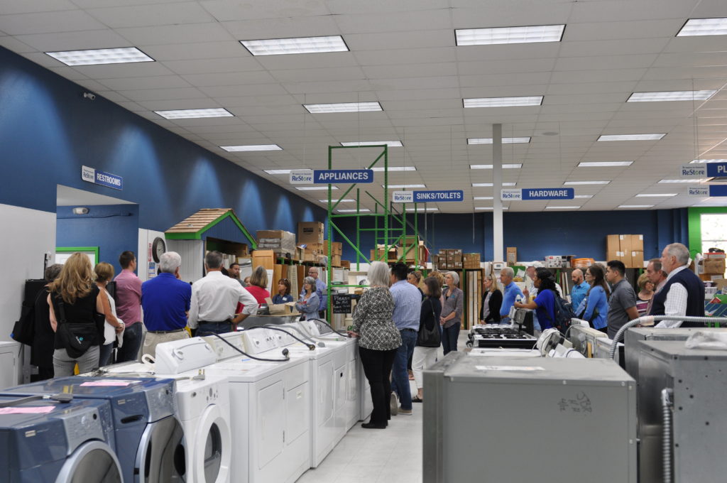 A group of people gather for a tour inside the Habitat for Humanity of North Idaho ReStore facility, with appliances and hardware around the room.