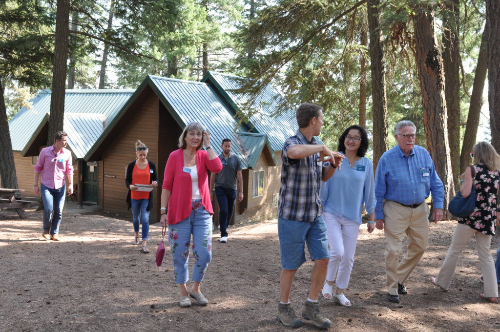 A group of people walk across a camp facility in the woods.