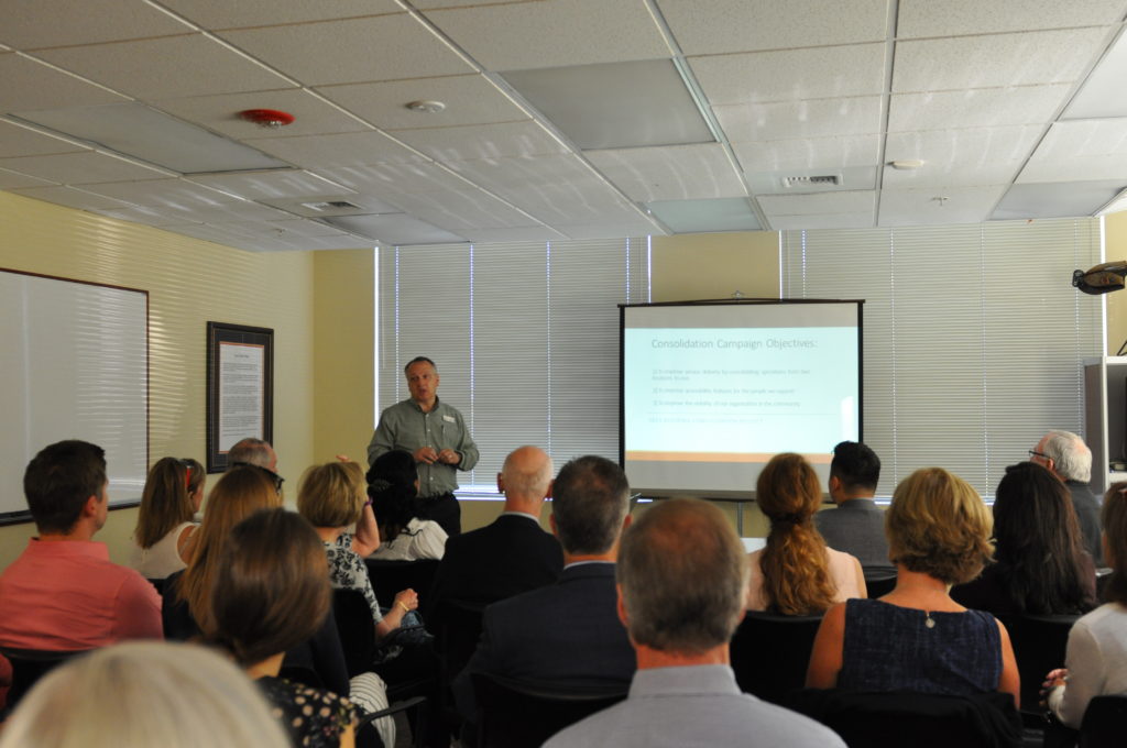 Staff at the Arc of Spokane give a presentation in front of a group of people inside a yellow room.