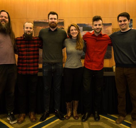 Six adults smile for the camera inside a room.