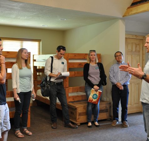 Four adults inside a camp bedroom on a tour of camp facilities.