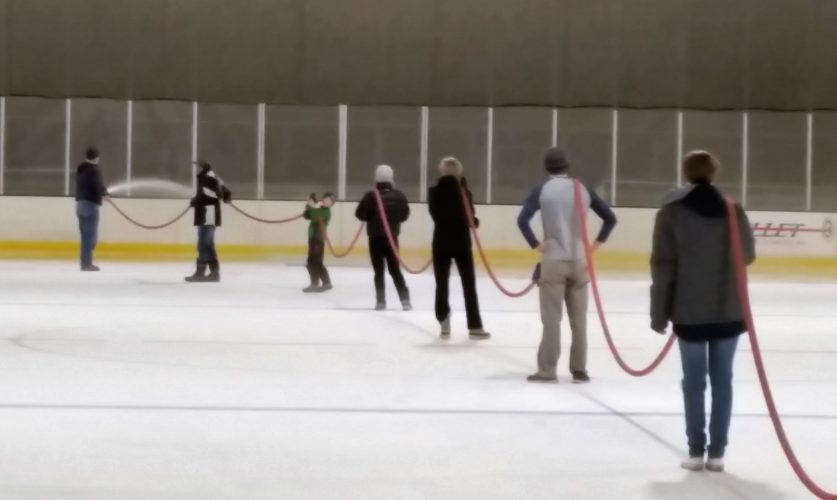 Eight volunteers holding a hose on an ice rink.