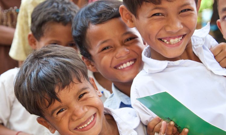 a close-up shot of four young boys with dark hair wearing white shirts smile for the camera.