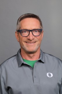 A man wearing a gray polo shirt and black glasses smiles at the camera.