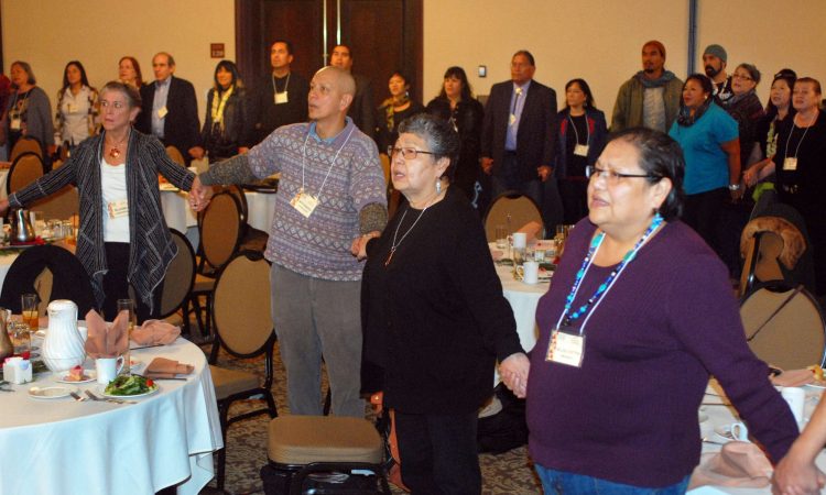 Adults join hands and stand in large circles inside a banquet hall.