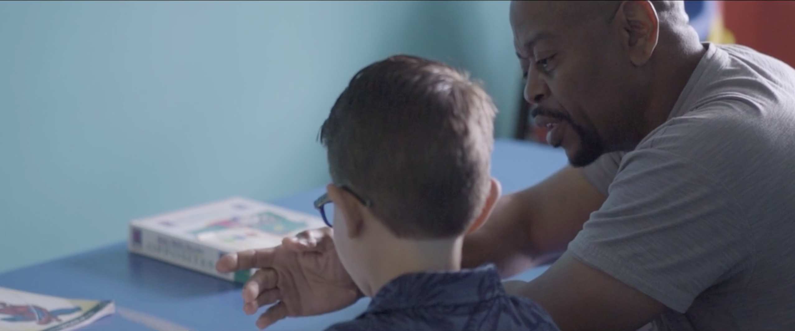 An adult man helps a young boy with homework.