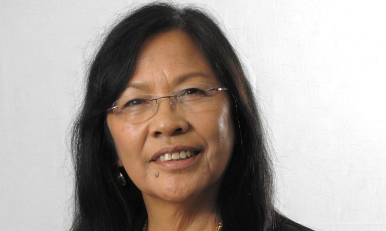 A woman with dark hair and glasses smiles at the camera.