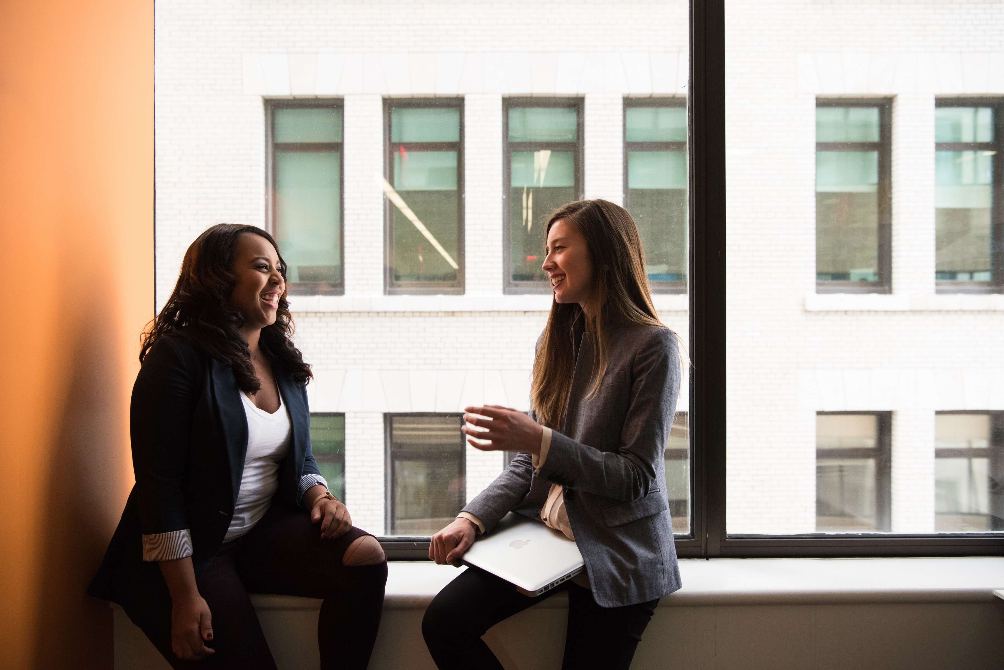 Two young women sitting near a window, laughing