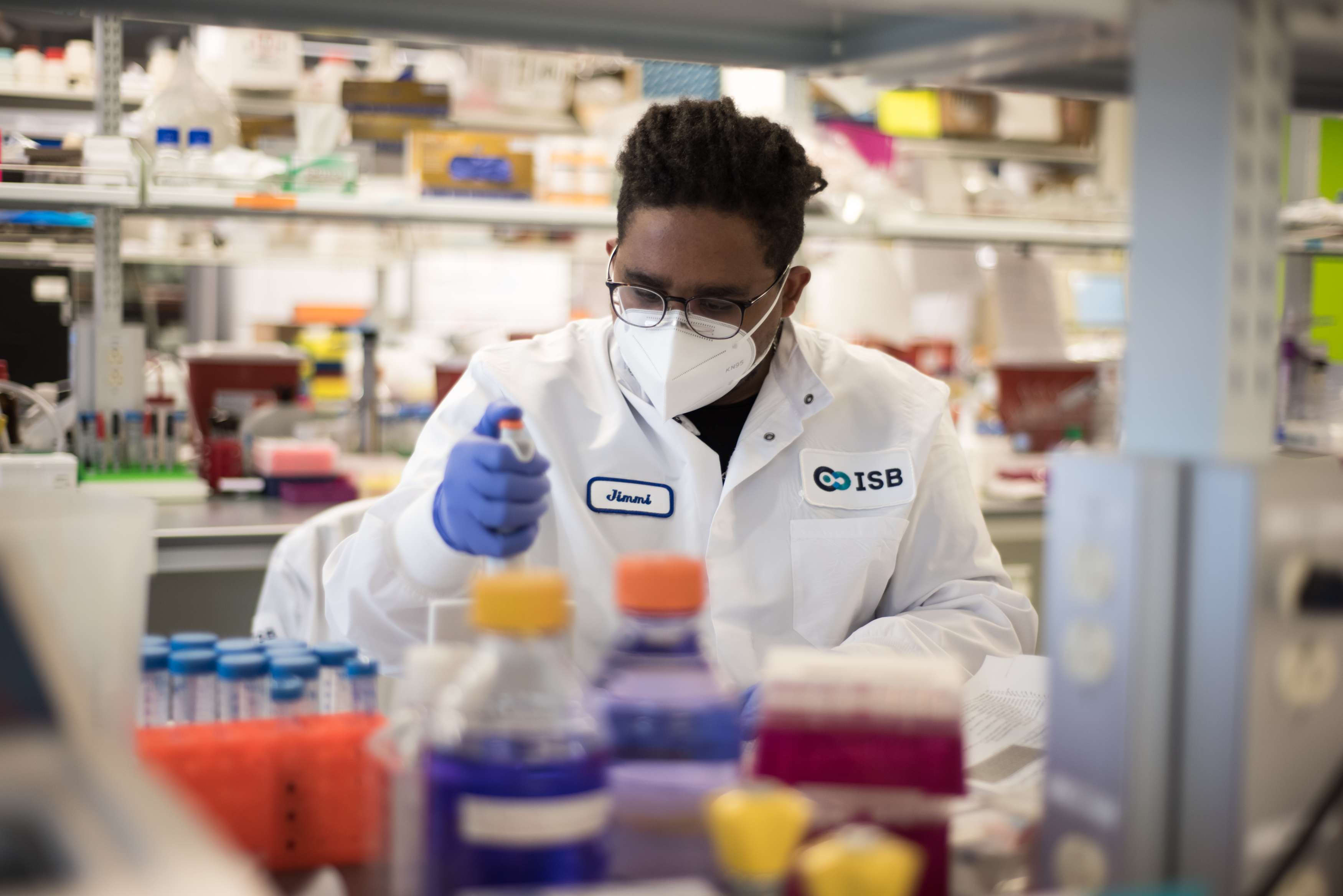 A man with black hair wearing a white lab coat in a scientific lab.