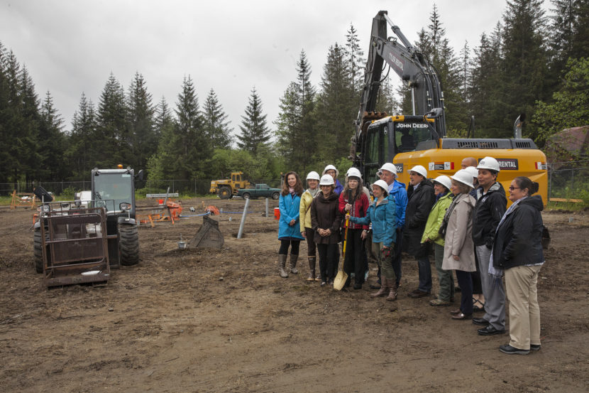 A group of adults wearing white hard hats stand in a construction site with tractors in the background.