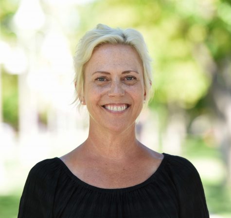 A woman with blond hair in a black shirt smiles at the camera while outside.