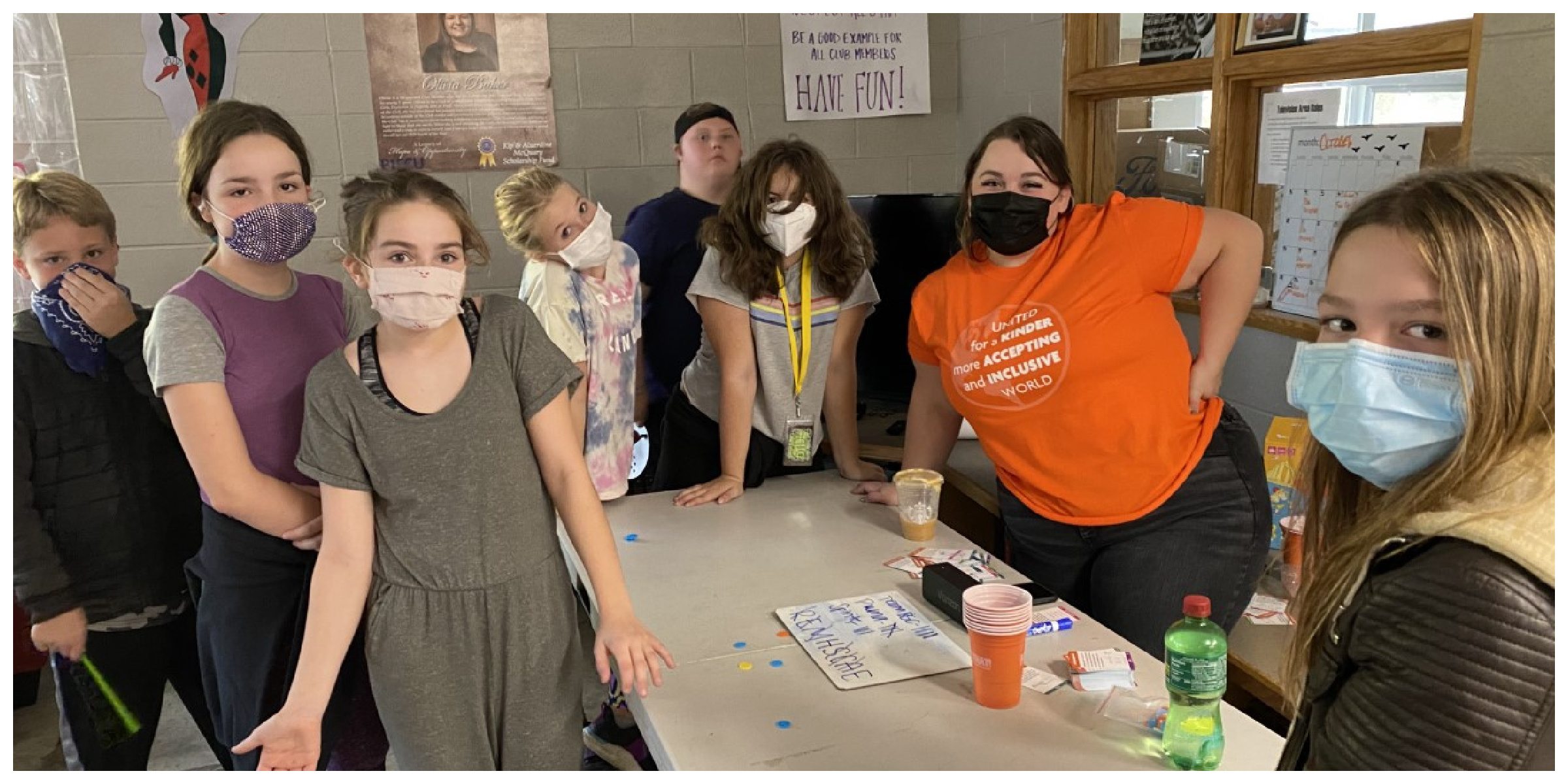 Eight children wearing masks pose for the camera around a table inside.