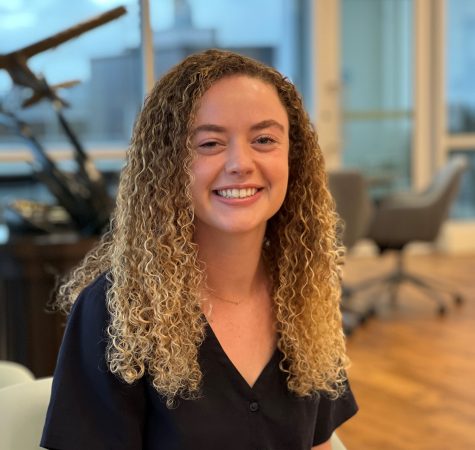 A woman with curly hair smiles at the camera inside an office.