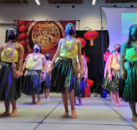 A group of dancers wearing colorful clothing, skirts, headbands, and necklaces inside a room with decorations.