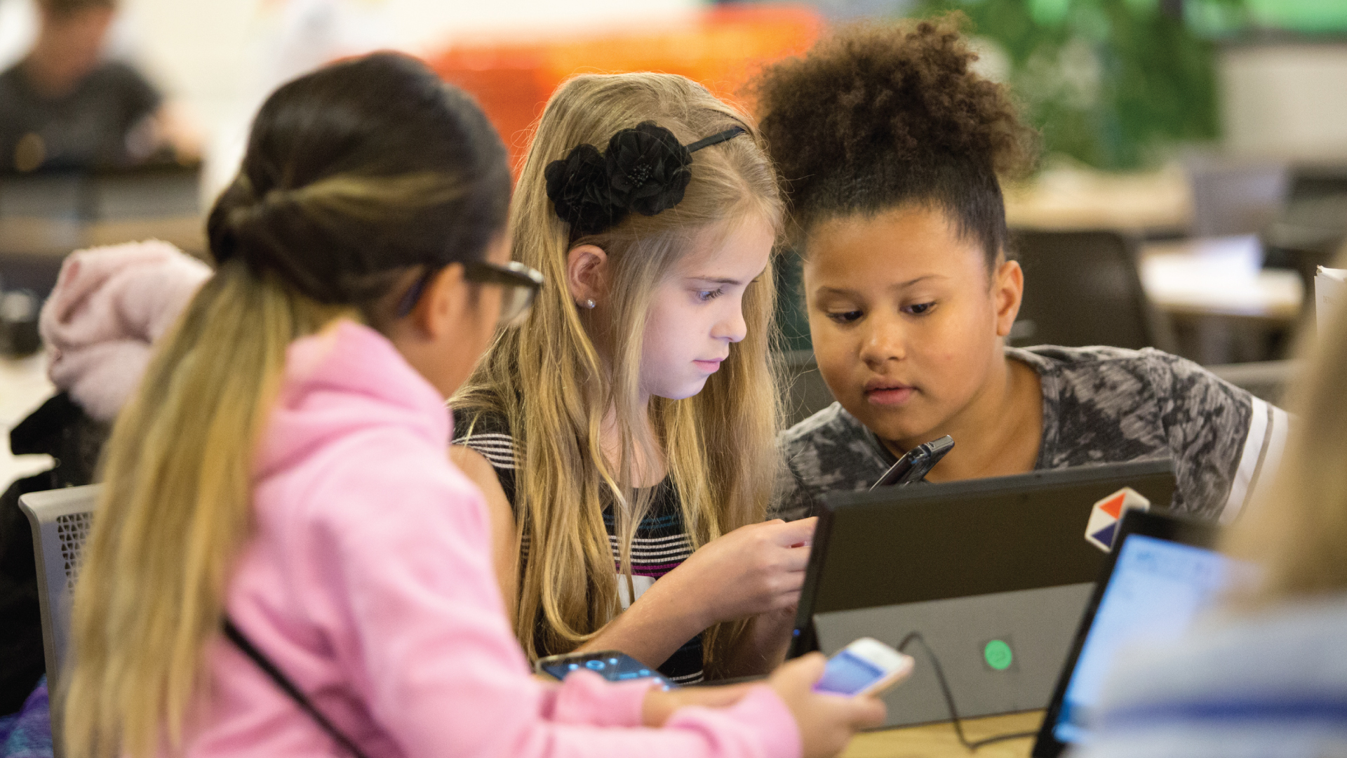 Three young girls look at a device.