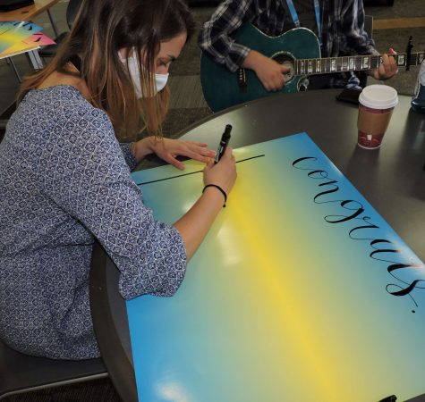 Woman with mask on writing on a poster that says congratulations