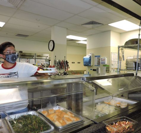 Man with mask serving food behind a heated food station