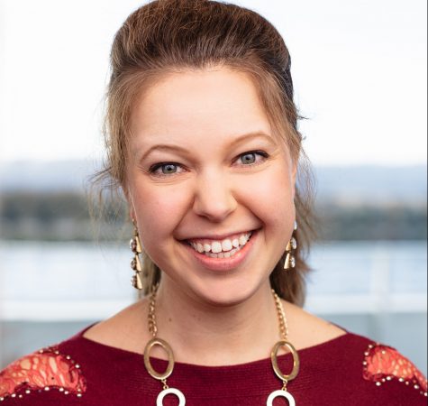 A woman with brown straight hair wearing a gold necklace and red shirt smiles for the camera