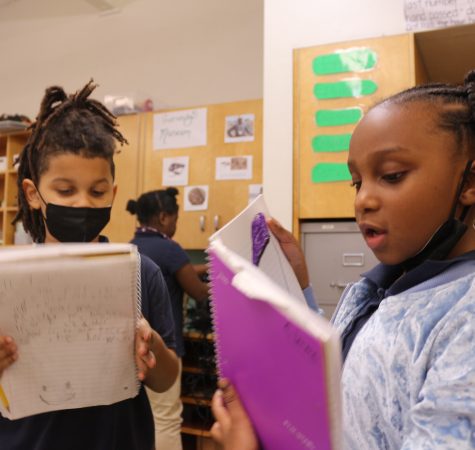 Two young students at KairosPDX read from notebooks inside a classroom.