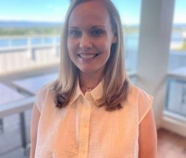 A woman with straight blond hair wearing a white shirt smiles at the camera.