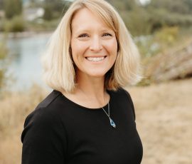 A woman with short blond hair wearing a black shirt smiles at the camera.