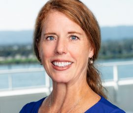 A woman with red hair wearing a blue shirt smiles for the camera.