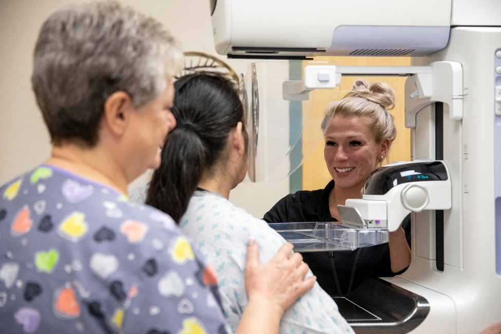 A nurse smiles at a patient near a 3D mammography equipment