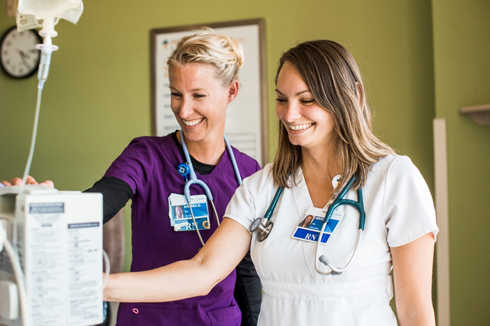 Two nurses smile while operating a 3D mammography machine