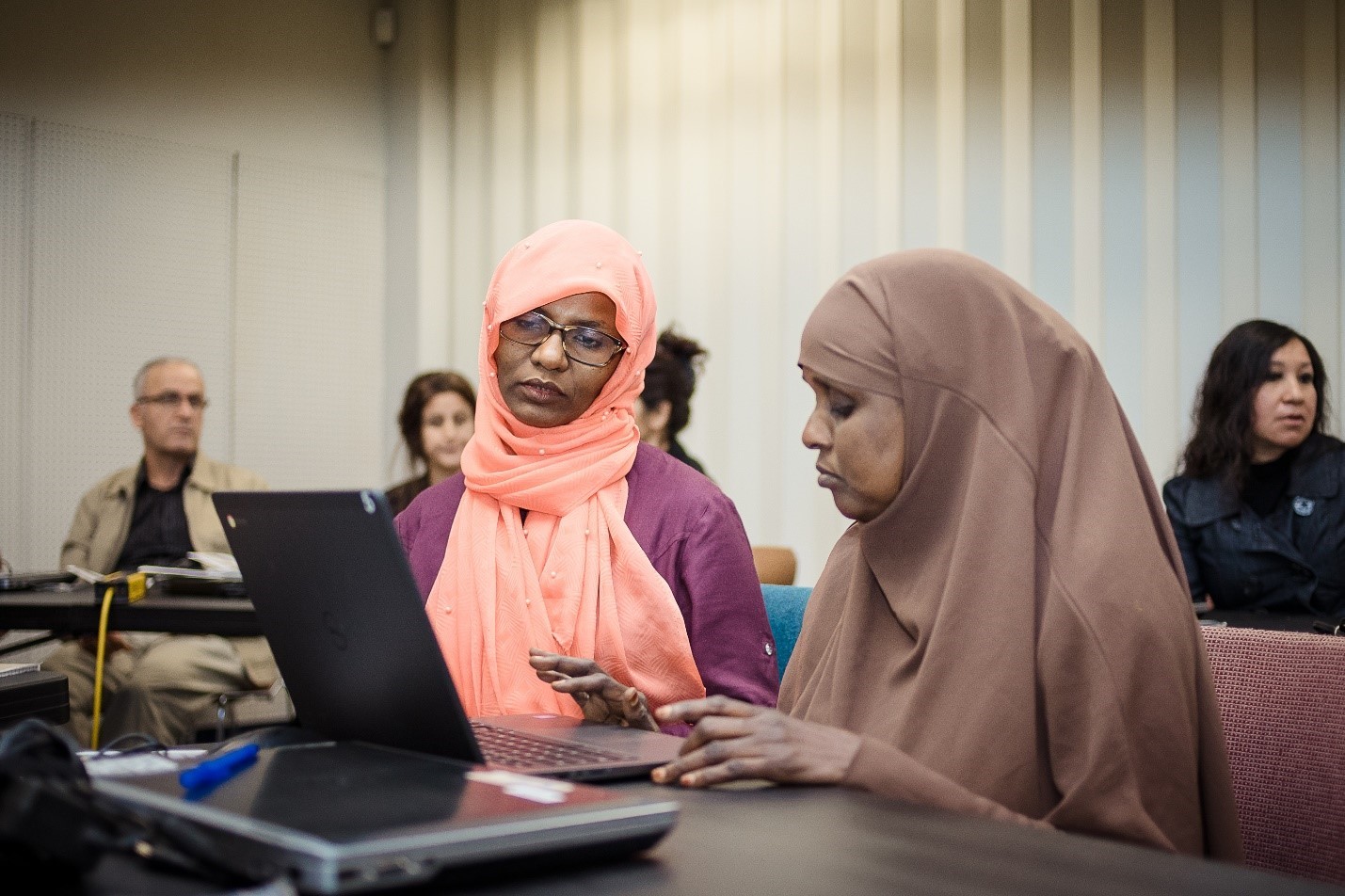 One woman typing on a laptop with another woman looking at the screen receiving tech education