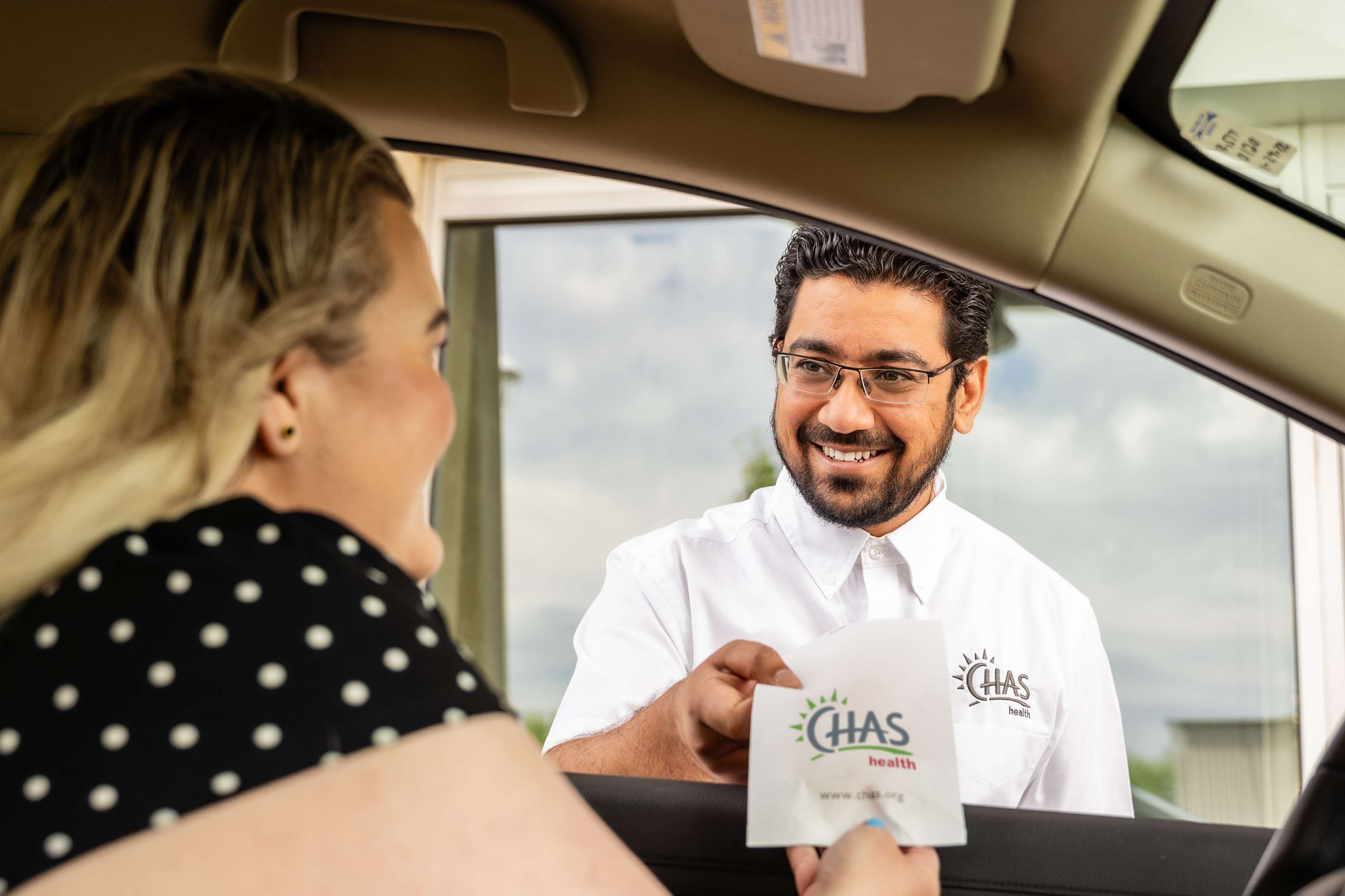 CHAS Health employee handing a prescription through a car window to a female patient