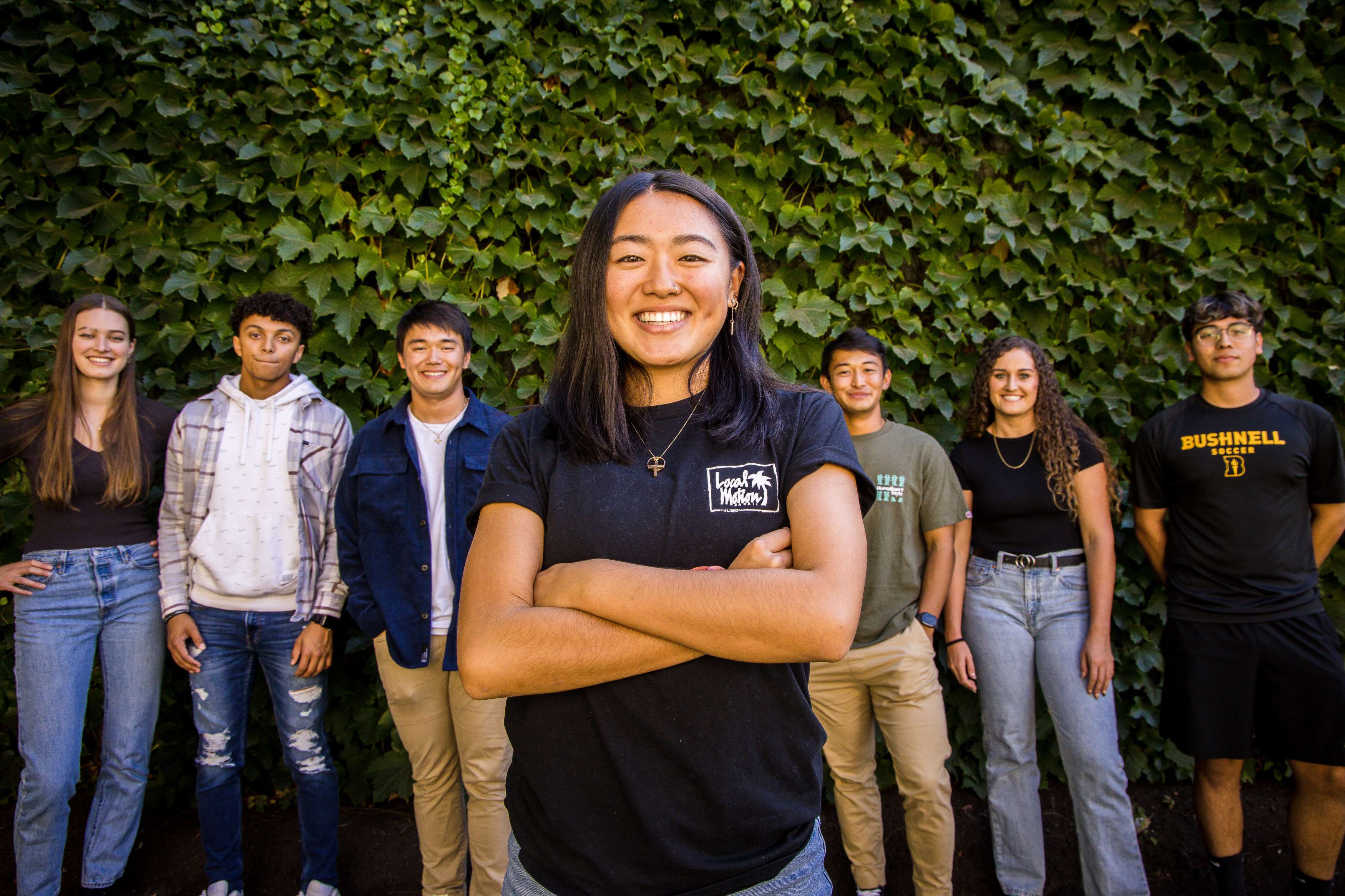 Female college student standing with arms crossed and smiling, with four other students behind her standing and smiling